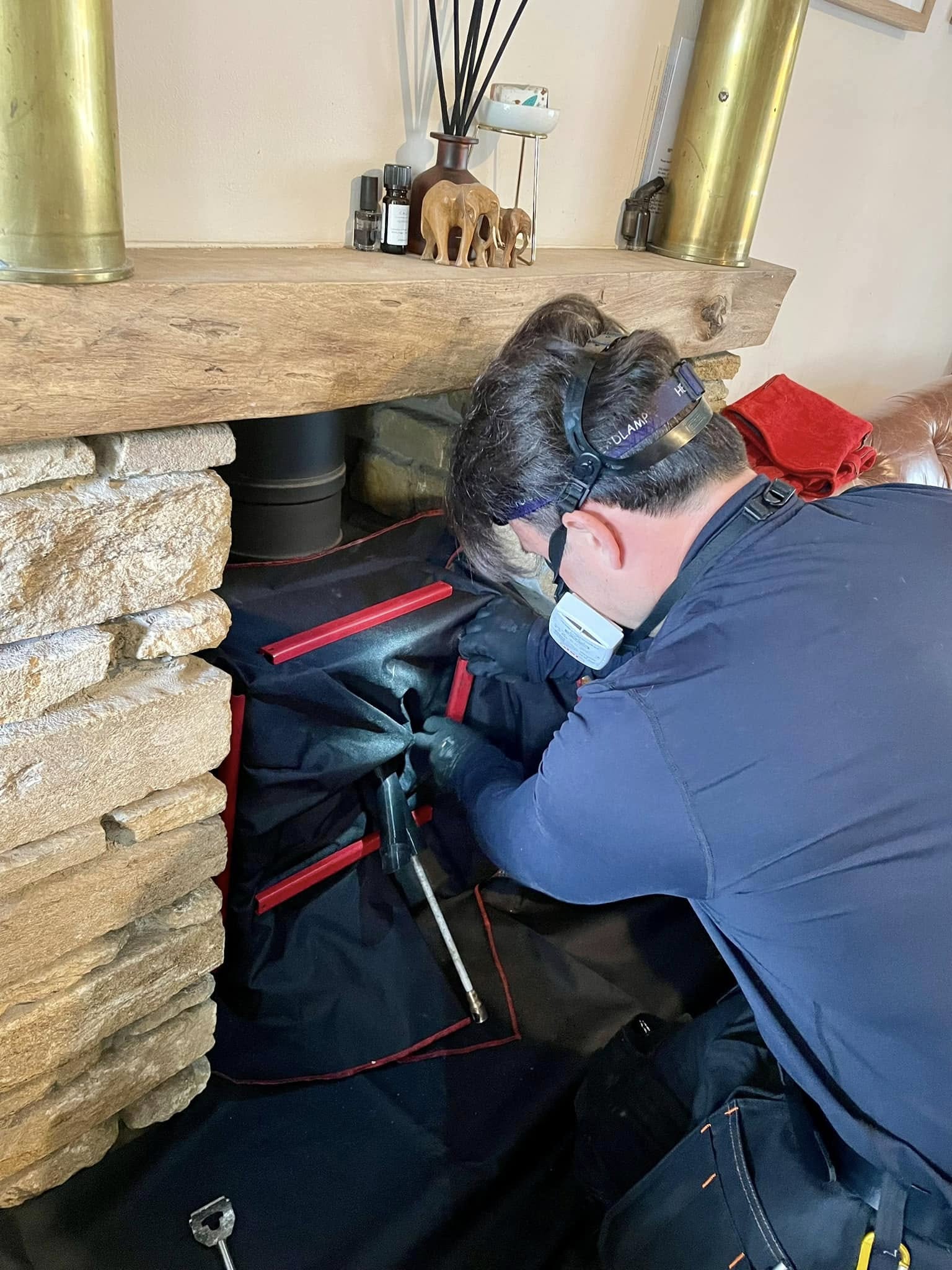 Graham kneeling at a stove under an oak beam with a head torch and mask