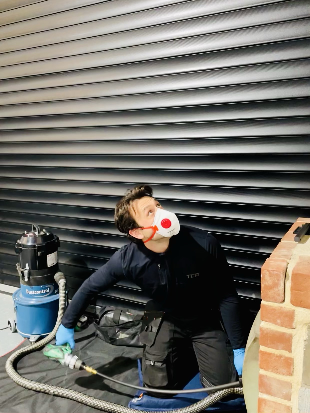 Graham in a dust mask with the sweeping vacuum at a brick fireplace