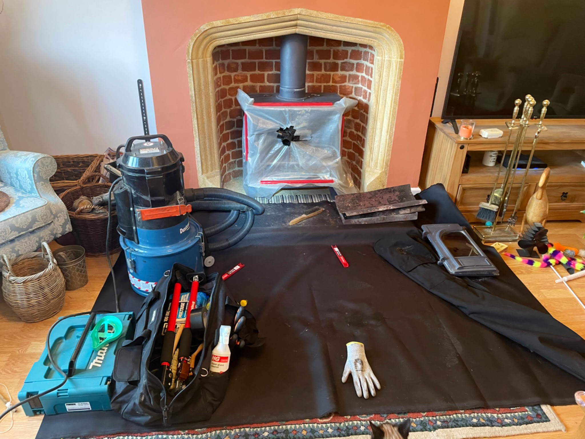 A stove in a stone inglenook sealed up, with the vacuum, tool bag and dust sheet laid out
