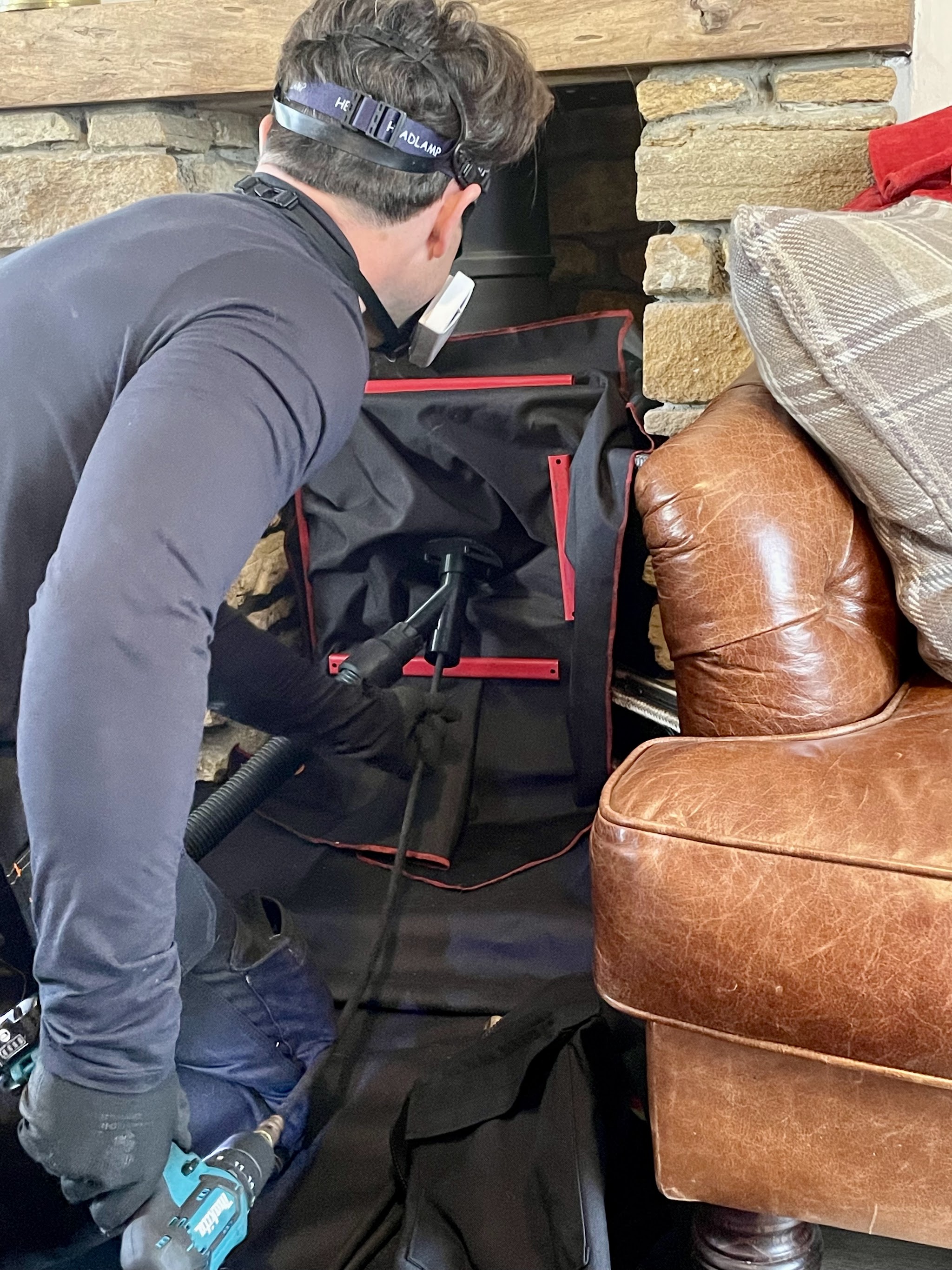 Graham sweeping a stove with the sweeping sheet and rods, beside a leather sofa